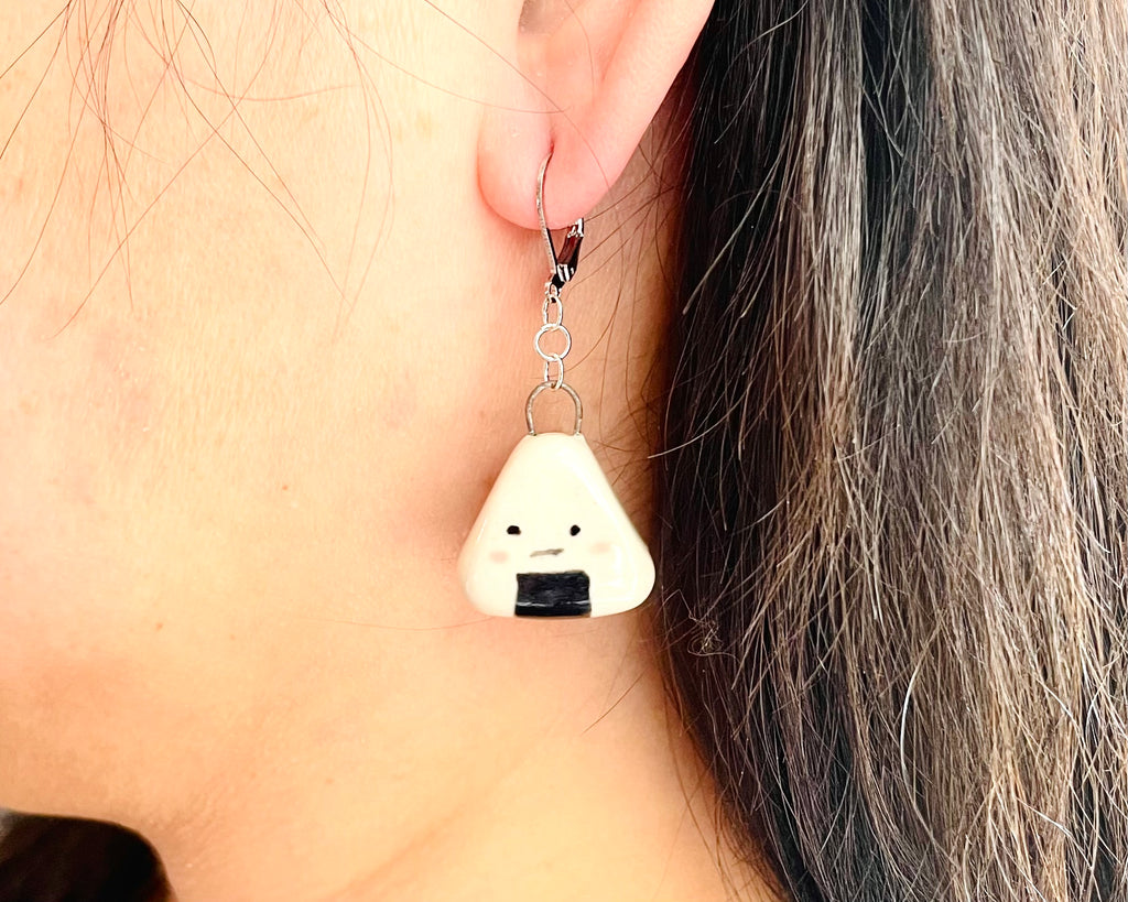 Earring shaped like a triangle with a black dot worn by a person with gray hair.