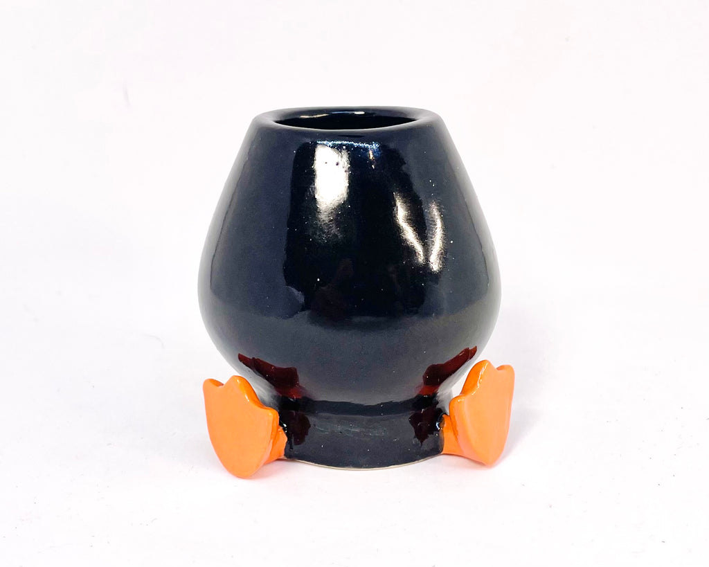 Black ceramic whisk holder with orange feet on a white background