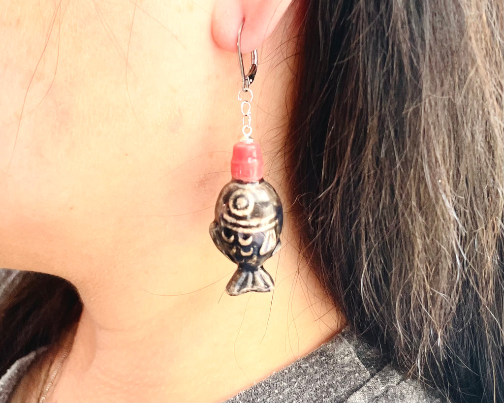 Close-up of an earring with a fish design hanging from an ear.