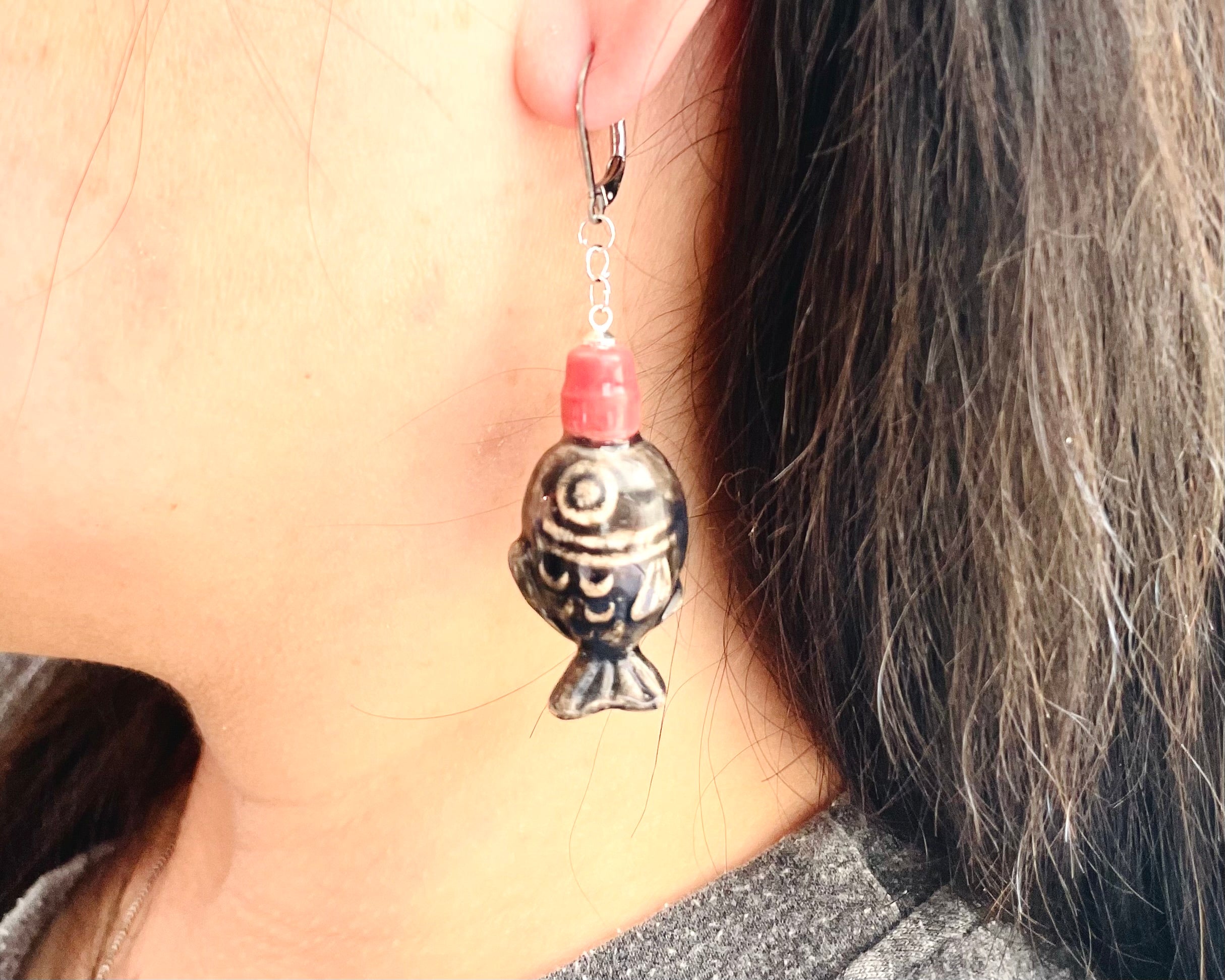 Close-up of an earring with a fish design hanging from an ear.