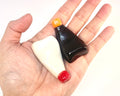 Hand holding two small bottles, one white and one black, with orange and red caps on a white background.